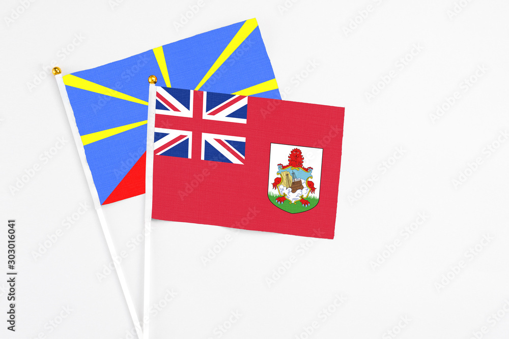 Fototapeta premium Bermuda and Reunion stick flags on white background. High quality fabric, miniature national flag. Peaceful global concept.White floor for copy space.