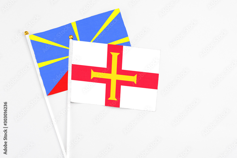Guernsey and Reunion stick flags on white background. High quality fabric, miniature national flag. Peaceful global concept.White floor for copy space.