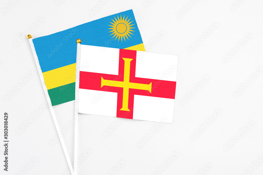 Guernsey and Rwanda stick flags on white background. High quality fabric, miniature national flag. Peaceful global concept.White floor for copy space.