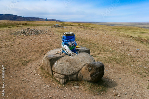 Stone turtle with sacred hadags or khadags (blue silk scarves) close to Erdene Zuu Khiid Monastery, UNESCO World Heritage Site, in Kharkhorin or Karakorum, Mongolia. photo