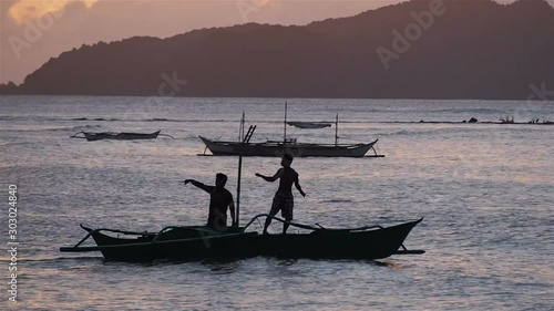 Silhouette of traditional filipino boat with two people moving around a beach near El Nido, Palawan, Philippines