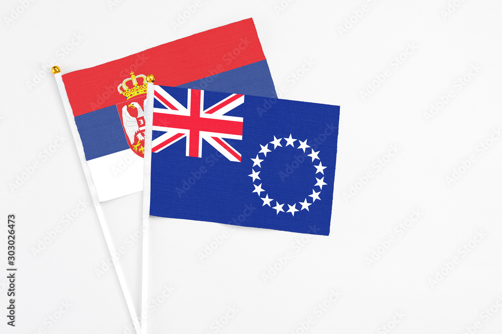 Fototapeta premium Cook Islands and Serbia stick flags on white background. High quality fabric, miniature national flag. Peaceful global concept.White floor for copy space.