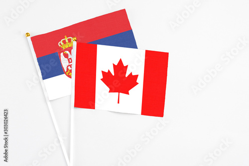 Canada and Serbia stick flags on white background. High quality fabric, miniature national flag. Peaceful global concept.White floor for copy space.