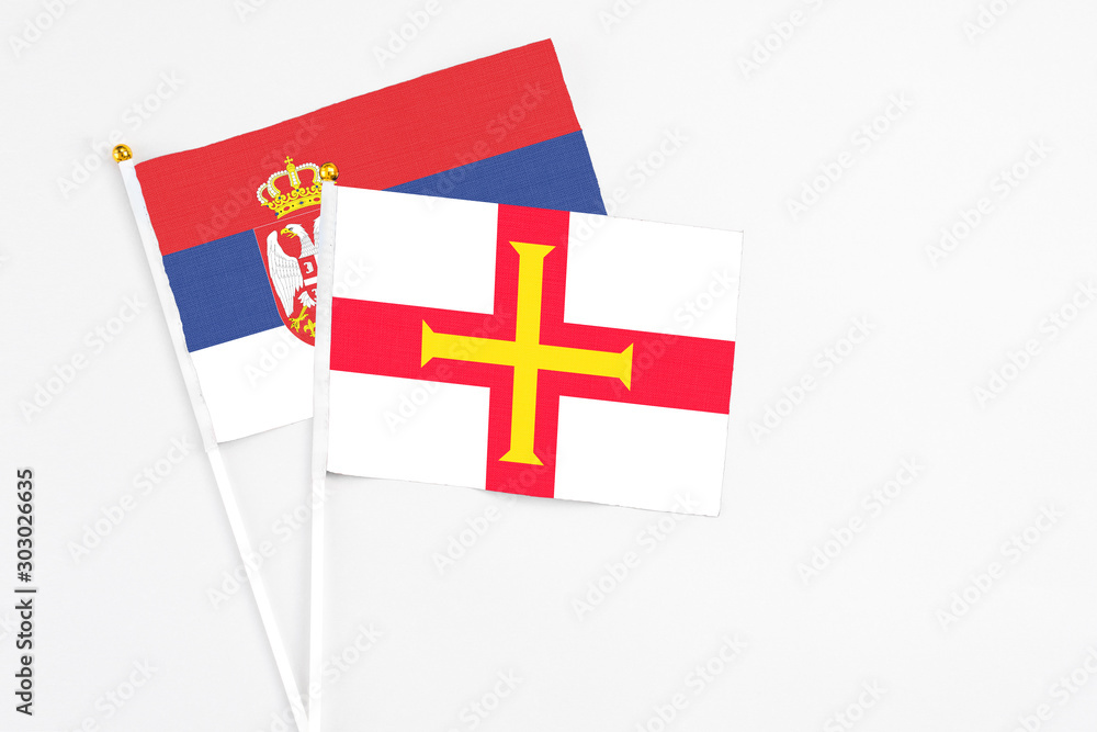 Guernsey and Serbia stick flags on white background. High quality fabric, miniature national flag. Peaceful global concept.White floor for copy space.