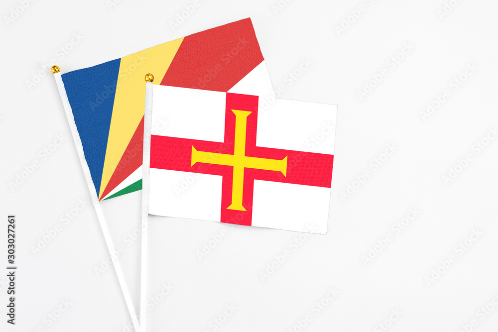 Guernsey and Seychelles stick flags on white background. High quality fabric, miniature national flag. Peaceful global concept.White floor for copy space.v