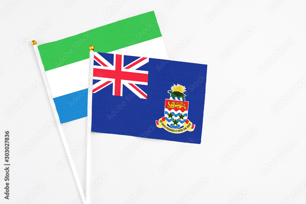Fototapeta premium Cayman Islands and Sierra Leone stick flags on white background. High quality fabric, miniature national flag. Peaceful global concept.White floor for copy space.