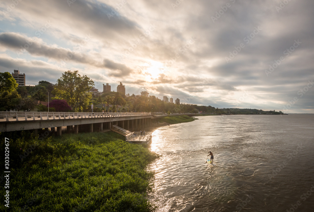person doing stand up paddle on the parana river with a beautiful sunset, clouds and colors