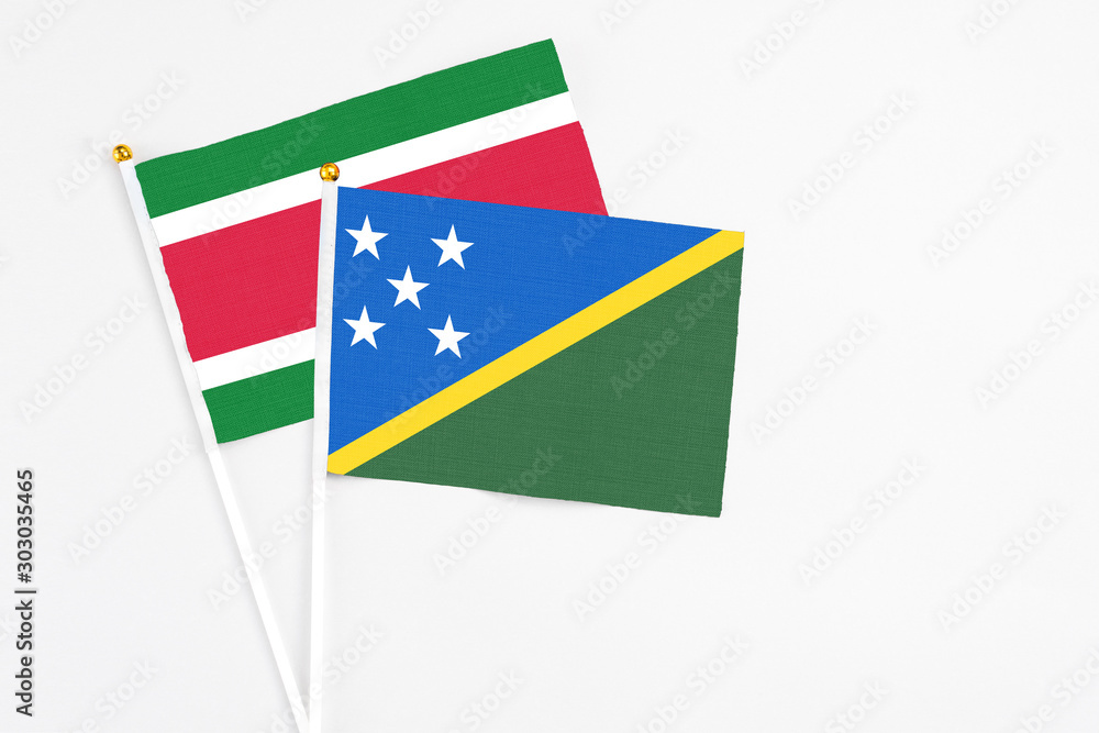 Solomon Islands and Suriname stick flags on white background. High quality fabric, miniature national flag. Peaceful global concept.White floor for copy space. Solomon Islands and Suriname stick flags on white background. High quality fabric, miniature national flag. Peaceful global concept.White floor for copy space.