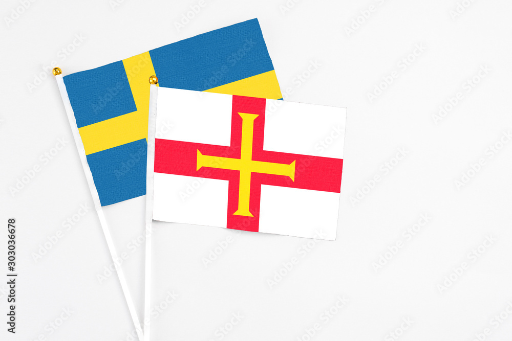 Guernsey and Sweden stick flags on white background. High quality fabric, miniature national flag. Peaceful global concept.White floor for copy space.