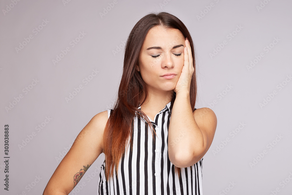 Close up image of cute woman has headache, keeps hands on temple, closes eyes, dressed casually, isolated over grey concrete wall. Desperate frustrated female has troubles, concentrates on solution. Close up image of cute woman has headache, keeps hands on temple, closes eyes, dressed casually, isolated over grey concrete wall. Desperate frustrated female has troubles, concentrates on solution.