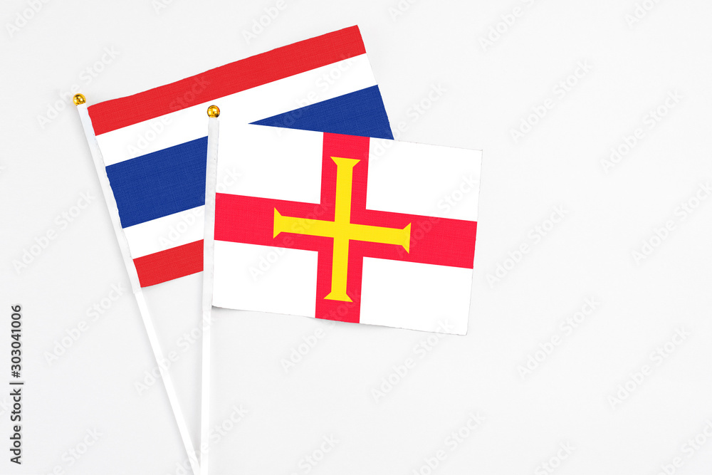 Guernsey and Thailand stick flags on white background. High quality fabric, miniature national flag. Peaceful global concept.White floor for copy space.