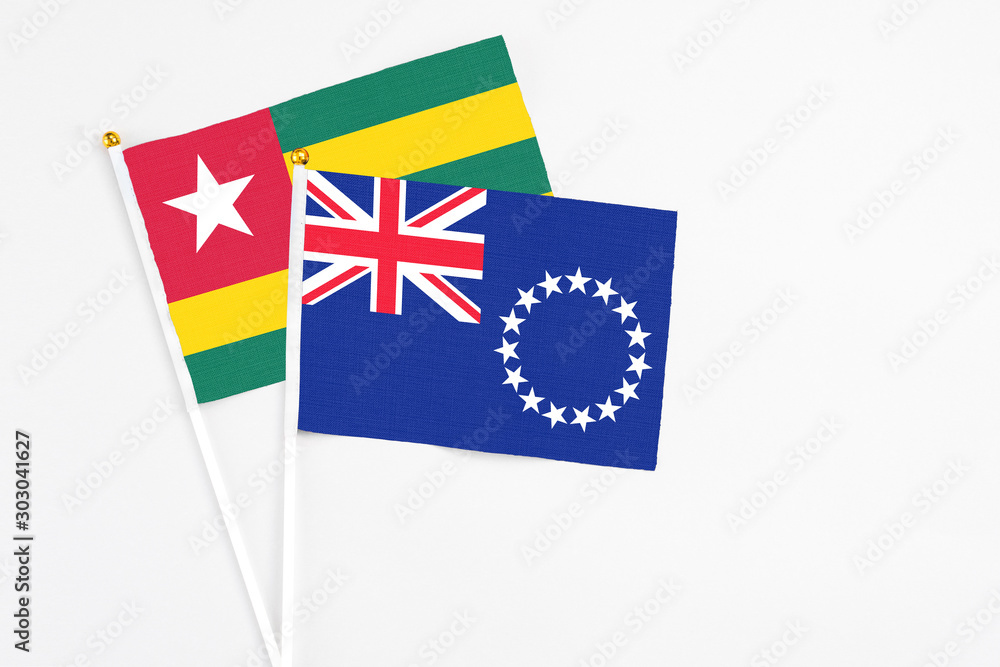 Fototapeta premium Cook Islands and Togo stick flags on white background. High quality fabric, miniature national flag. Peaceful global concept.White floor for copy space.