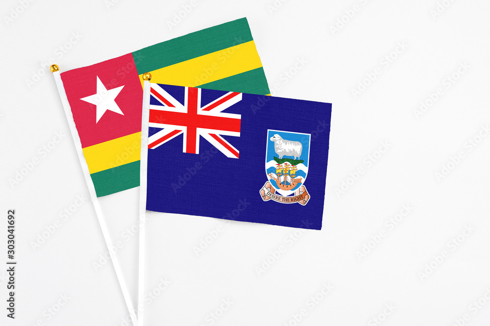 Fototapeta premium Falkland Islands and Togo stick flags on white background. High quality fabric, miniature national flag. Peaceful global concept.White floor for copy space.