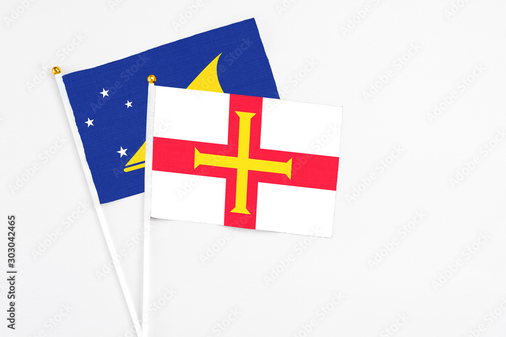 Guernsey and Tokelau stick flags on white background. High quality fabric, miniature national flag. Peaceful global concept.White floor for copy space.