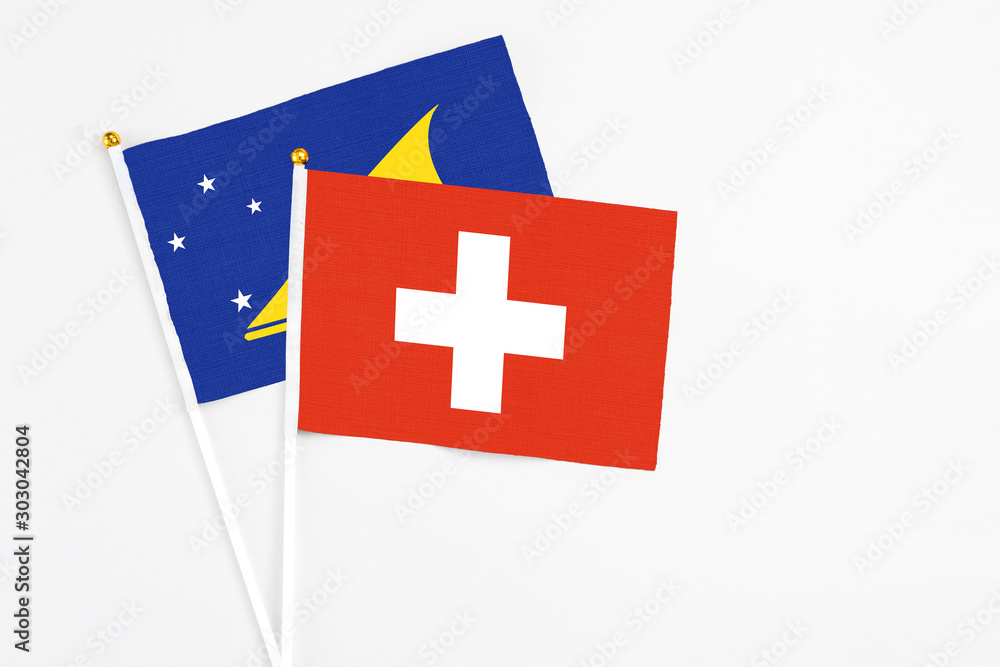 Switzerland and Tokelau stick flags on white background. High quality fabric, miniature national flag. Peaceful global concept.White floor for copy space.