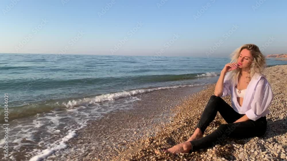 Beautiful blonde woman sitting and meditating on the beach near the waves of blue sea.Crimea, Sevastopol. Beautiful blonde woman sitting and meditating on the beach near the waves of blue sea.Crimea, Sevastopol.