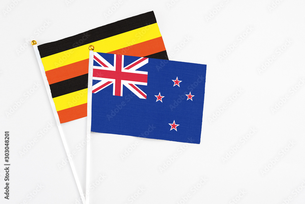 Fototapeta premium New Zealand and Uganda stick flags on white background. High quality fabric, miniature national flag. Peaceful global concept.White floor for copy space.