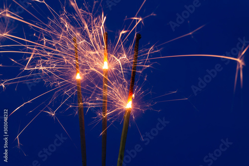 Three burning sparklers on blue background close up