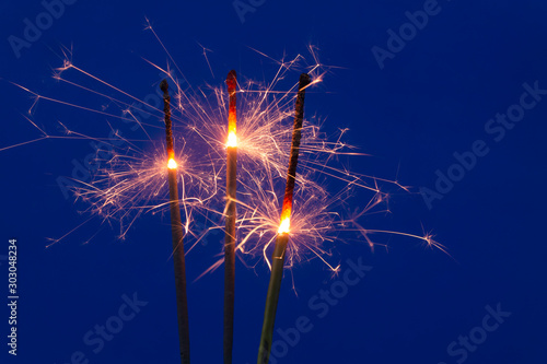 Three burning sparklers on blue background