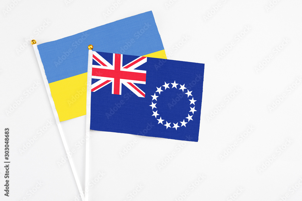Fototapeta premium Cook Islands and Ukraine stick flags on white background. High quality fabric, miniature national flag. Peaceful global concept.White floor for copy space.