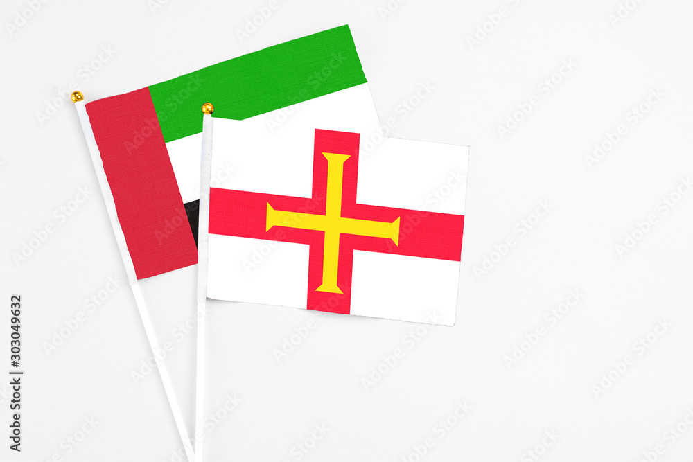 Guernsey and United Arab Emirates stick flags on white background. High quality fabric, miniature national flag. Peaceful global concept.White floor for copy space.