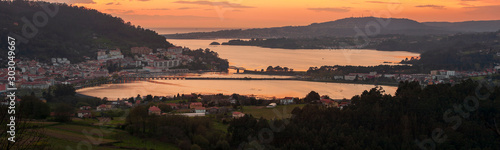 Serene dusk panorama of the medieval fishing town of Pontedeume with its iron and stone bridge orange sky La Coru  a Galicia