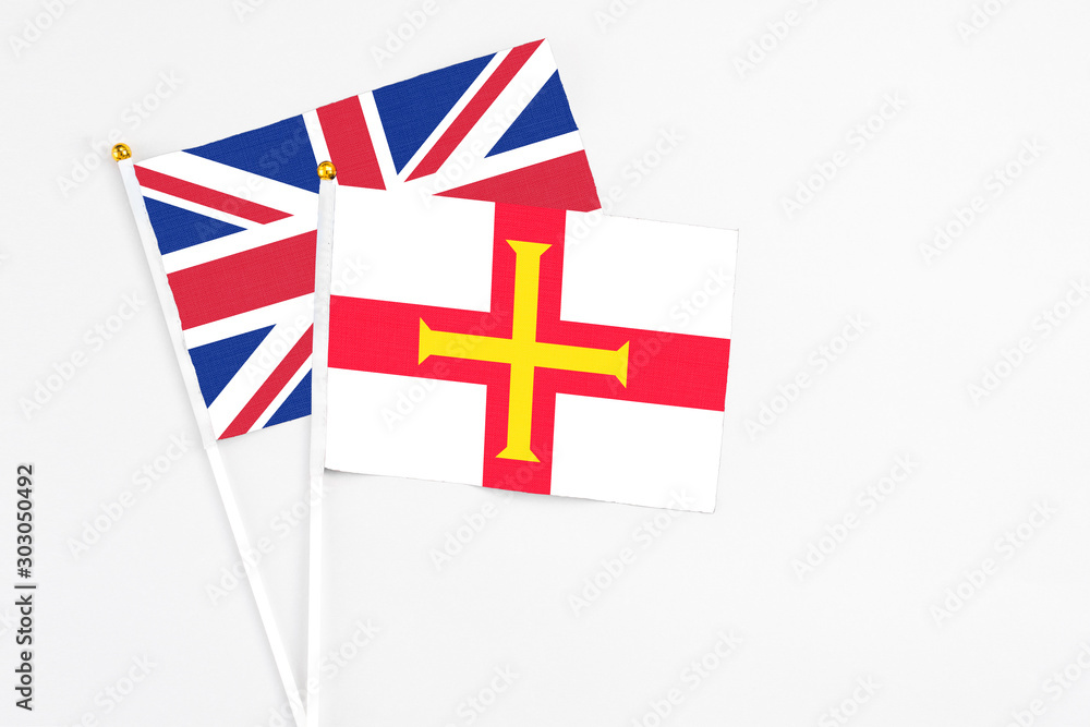 Fototapeta premium Guernsey and United Kingdom stick flags on white background. High quality fabric, miniature national flag. Peaceful global concept.White floor for copy space.