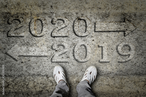 2020 and 2019 with direction arrows written on an concrete flooring with male feet standing.