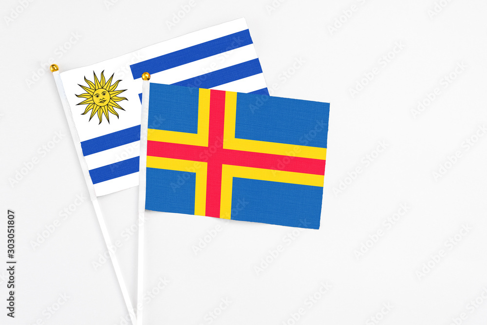 Aland Islands and Uruguay stick flags on white background. High quality fabric, miniature national flag. Peaceful global concept.White floor for copy space.