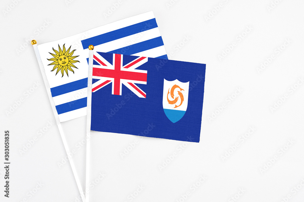 Fototapeta premium Anguilla and Uruguay stick flags on white background. High quality fabric, miniature national flag. Peaceful global concept.White floor for copy space.