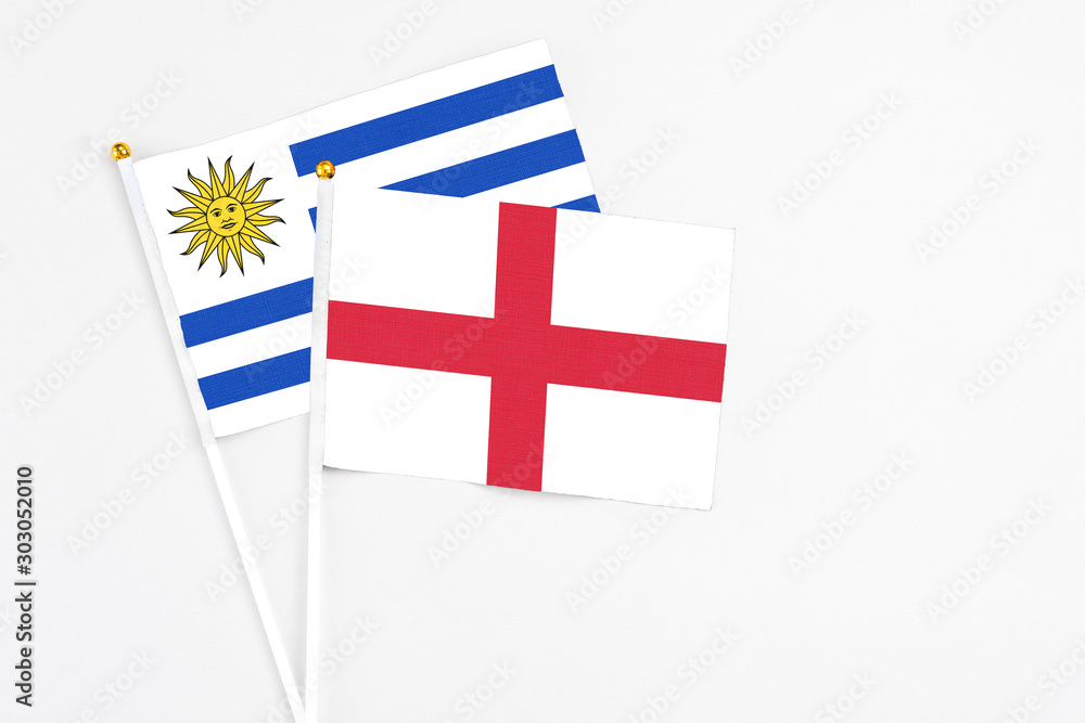 England and Uruguay stick flags on white background. High quality fabric, miniature national flag. Peaceful global concept.White floor for copy space.