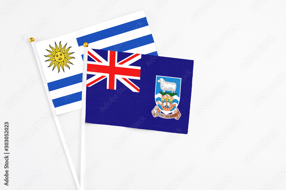 Fototapeta premium Falkland Islands and Uruguay stick flags on white background. High quality fabric, miniature national flag. Peaceful global concept.White floor for copy space.
