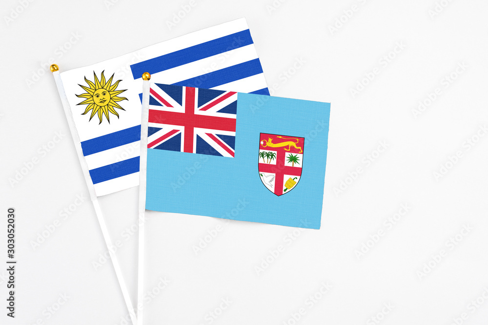 Fototapeta premium Fiji and Uruguay stick flags on white background. High quality fabric, miniature national flag. Peaceful global concept.White floor for copy space.