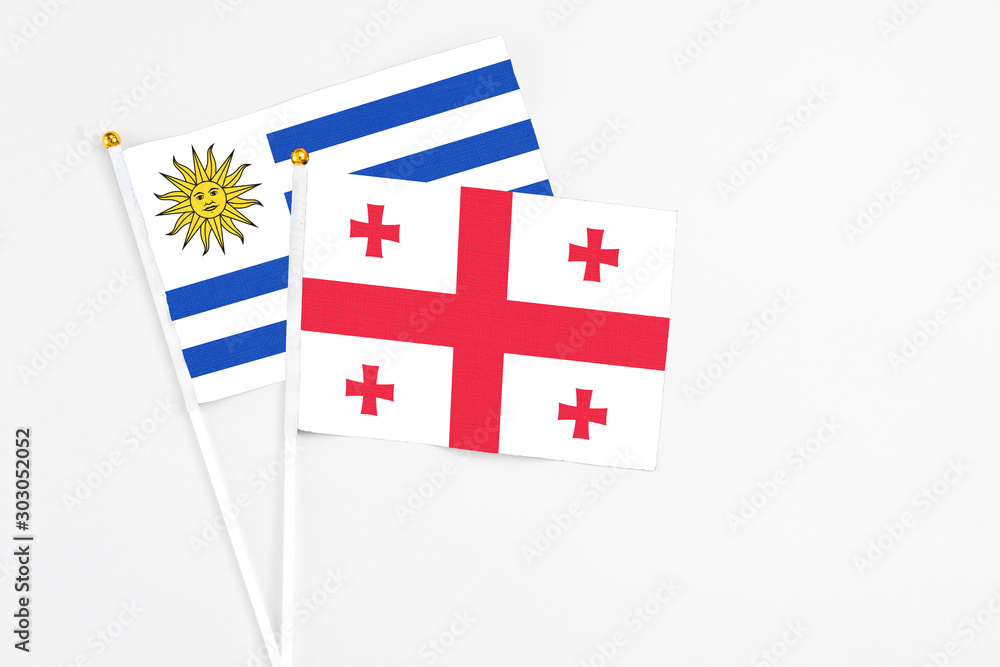 Georgia and Uruguay stick flags on white background. High quality fabric, miniature national flag. Peaceful global concept.White floor for copy space.
