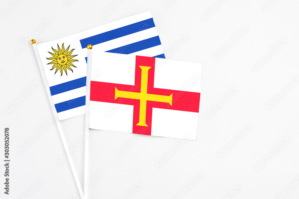 Guernsey and Uruguay stick flags on white background. High quality fabric, miniature national flag. Peaceful global concept.White floor for copy space.