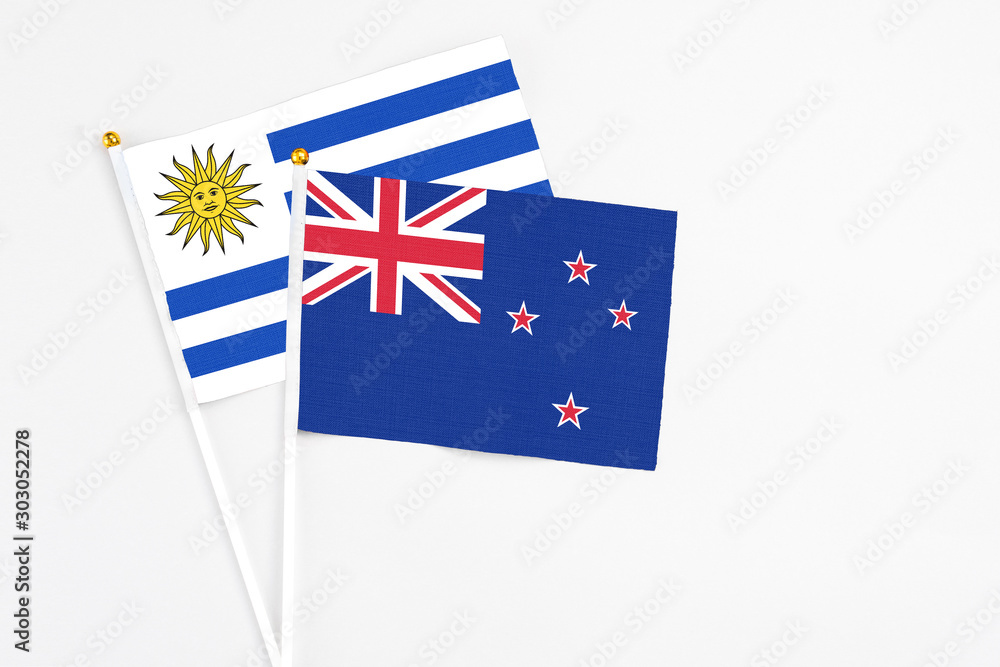 Fototapeta premium New Zealand and Uruguay stick flags on white background. High quality fabric, miniature national flag. Peaceful global concept.White floor for copy space.