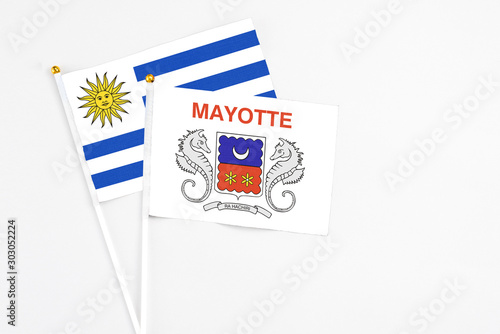 Mayotte and Uruguay stick flags on white background. High quality fabric, miniature national flag. Peaceful global concept.White floor for copy space.