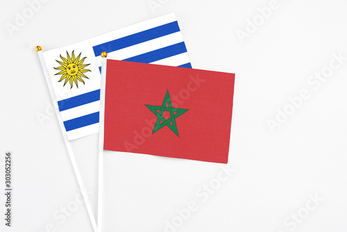 Morocco and Uruguay stick flags on white background. High quality fabric, miniature national flag. Peaceful global concept.White floor for copy space.