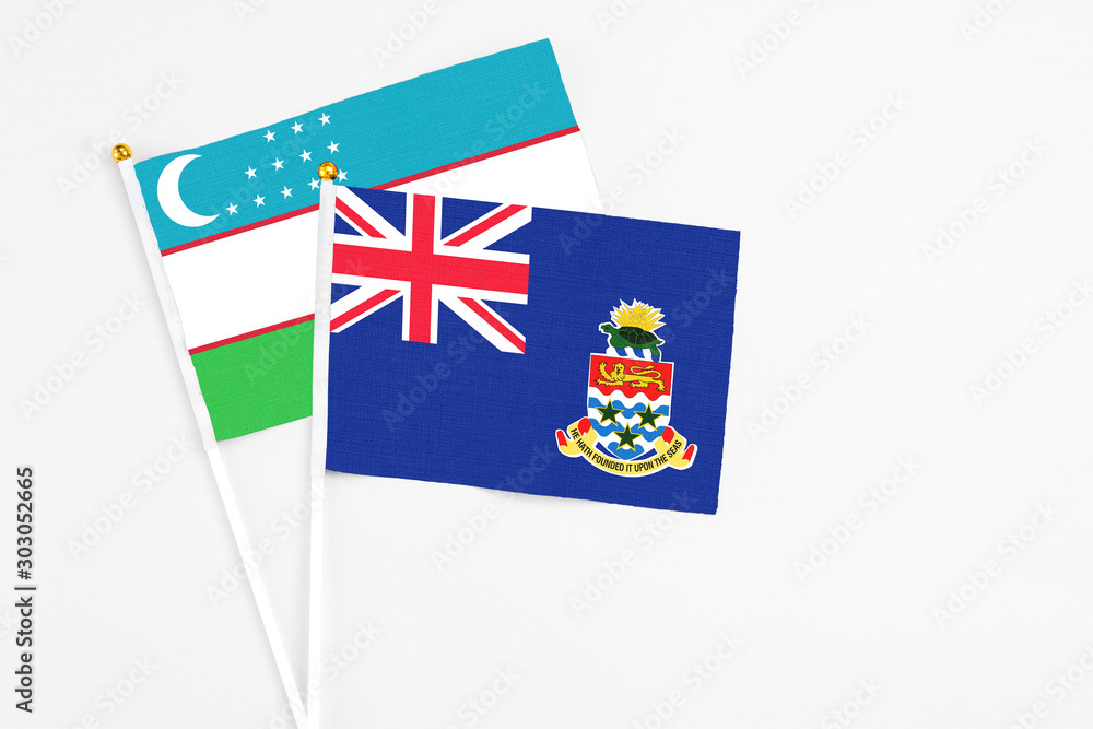Fototapeta premium Cayman Islands and Uzbekistan stick flags on white background. High quality fabric, miniature national flag. Peaceful global concept.White floor for copy space.