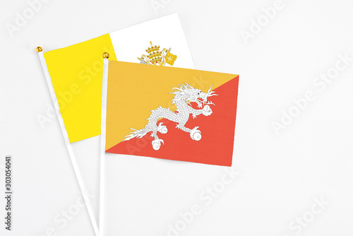Bhutan and Vatican City stick flags on white background. High quality fabric, miniature national flag. Peaceful global concept.White floor for copy space.