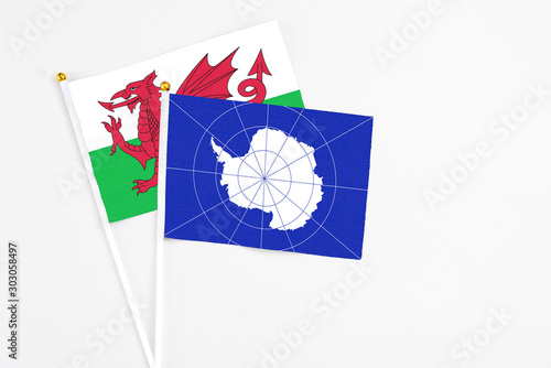 Antarctica and Wales stick flags on white background. High quality fabric, miniature national flag. Peaceful global concept.White floor for copy space.