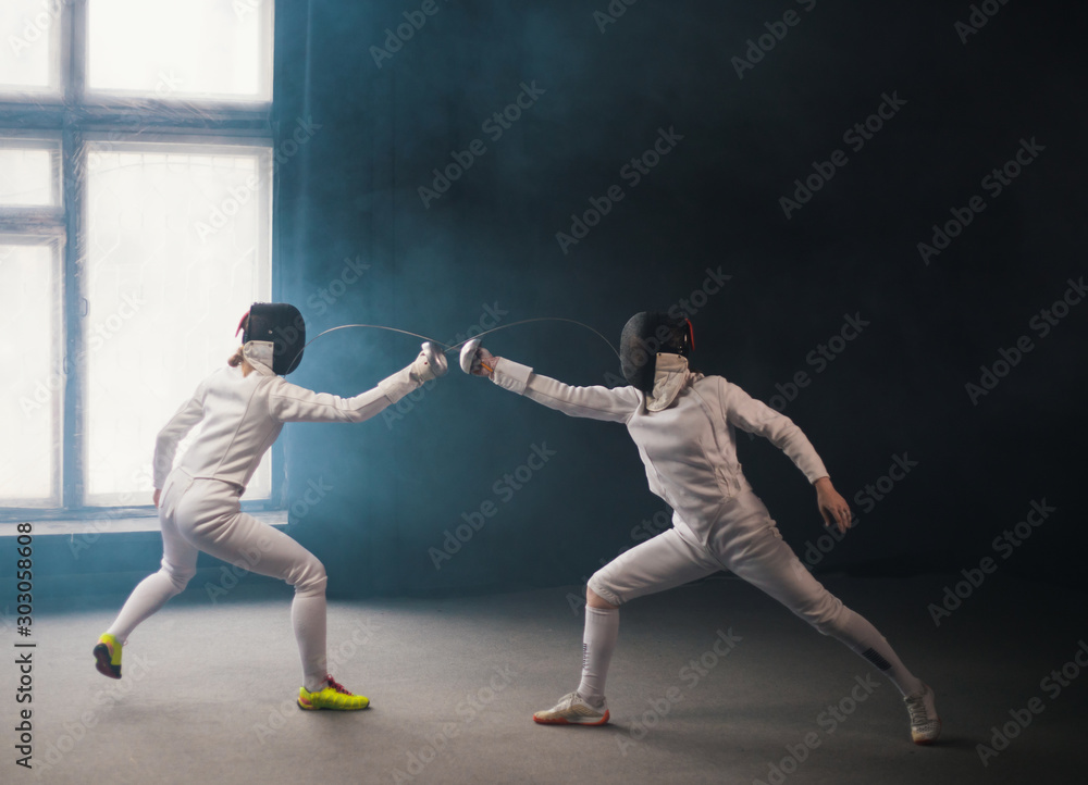 A fencing training in the studio - two women in protective costumes having a duel - poking with a swords in each other