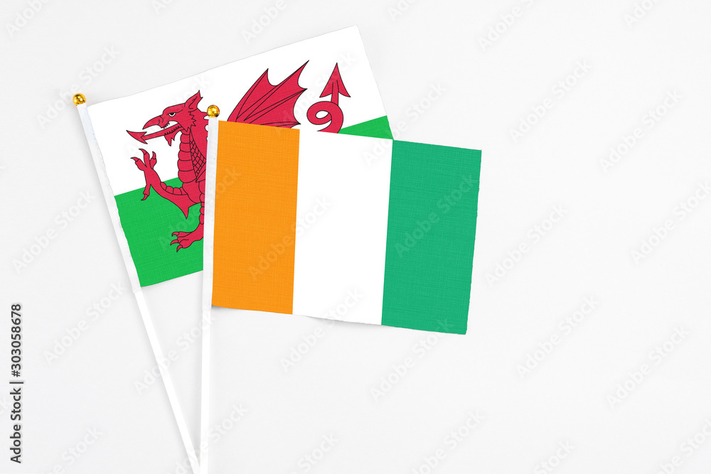 Cote D'Ivoire and Wales stick flags on white background. High quality fabric, miniature national flag. Peaceful global concept.White floor for copy space. Cote D'Ivoire and Wales stick flags on white background. High quality fabric, miniature national flag. Peaceful global concept.White floor for copy space.