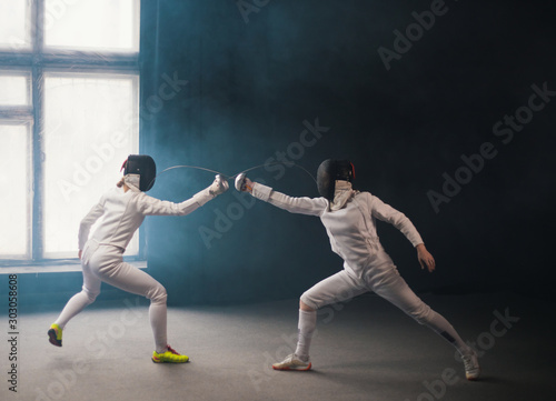 A fencing training in the studio - two women in protective costumes having a duel - poking with a swords in each other