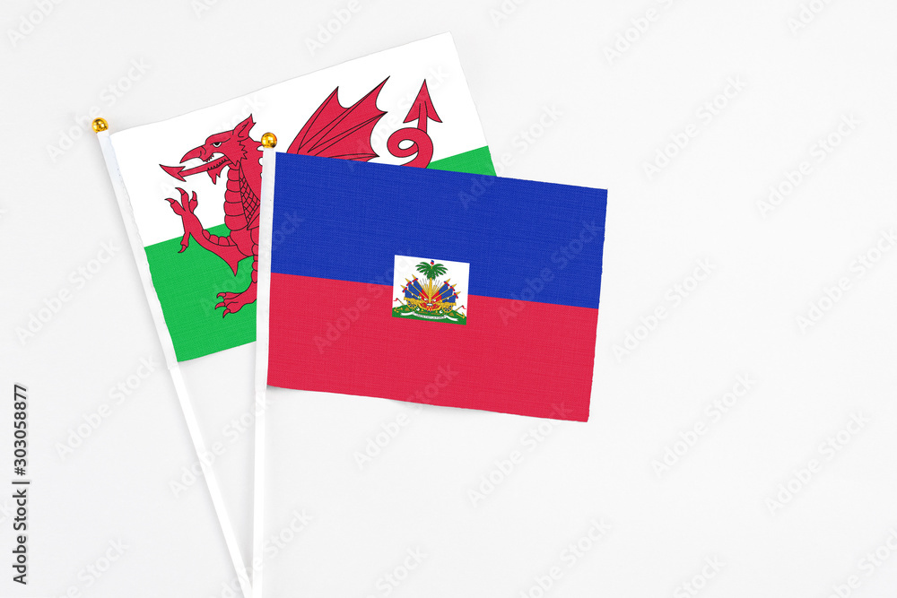 Haiti and Wales stick flags on white background. High quality fabric, miniature national flag. Peaceful global concept.White floor for copy space.