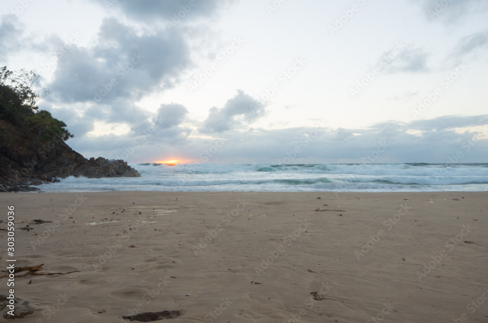 Sun rising over the horizon at a beach by a headland Sun rising over the horizon at a beach by a headland