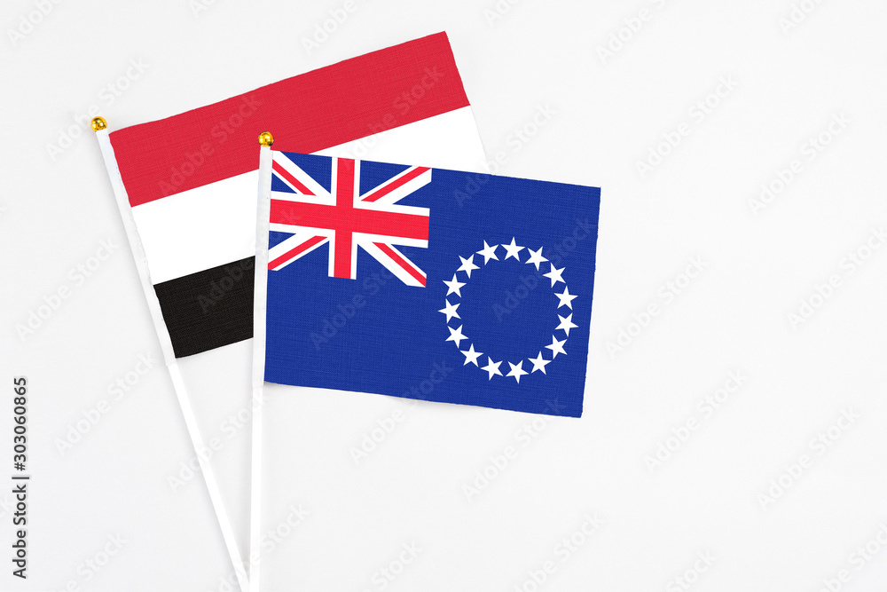 Fototapeta premium Cook Islands and Yemen stick flags on white background. High quality fabric, miniature national flag. Peaceful global concept.White floor for copy space.