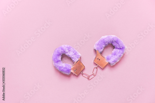 Handcuffs with purple hair adult sex toys, minimal design, isolated on a pink background.