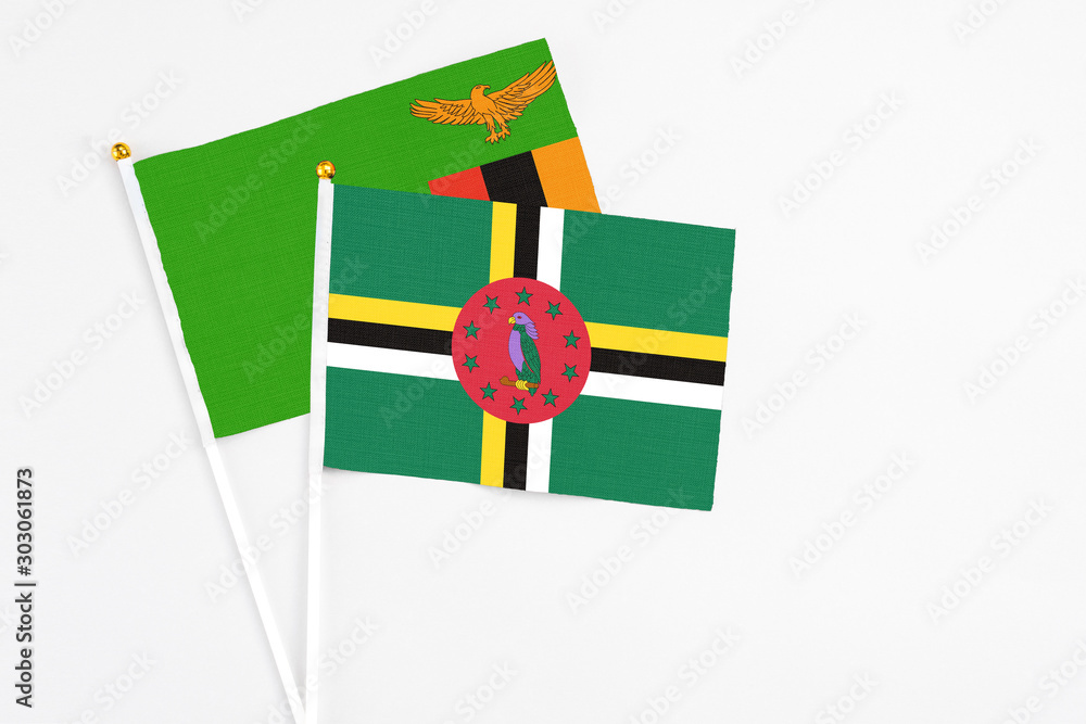 Fototapeta premium Dominica and Zambia stick flags on white background. High quality fabric, miniature national flag. Peaceful global concept.White floor for copy space.