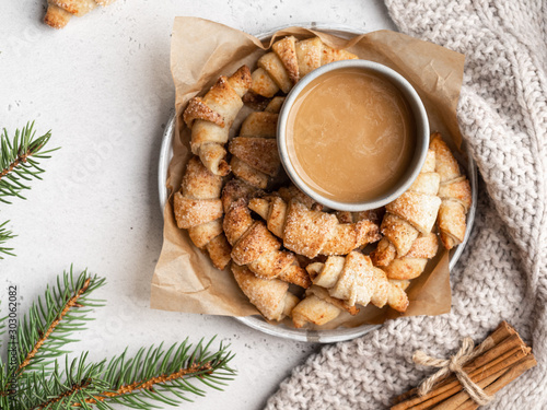 Homemade christmas croissants (crescent rolls) on a wooden tray with fir tree branches and cinnamon sticks . Christmas and new year background, layout template.
